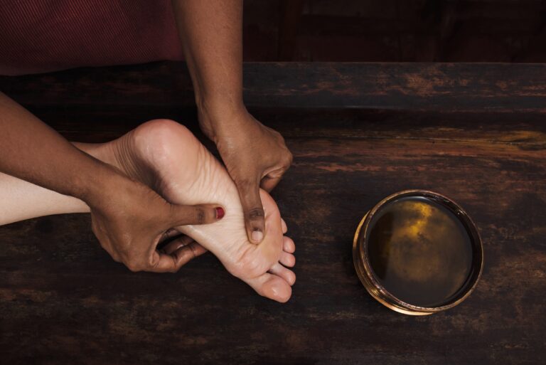 Ayurvedic foot massage with oil on the wooden table in traditional style made by asian women. Top view.